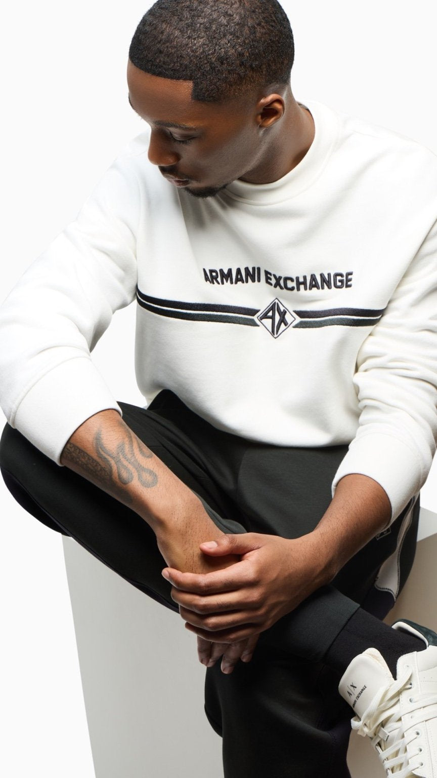 Person wearing an Armani Exchange sweatshirt sitting on a white box.