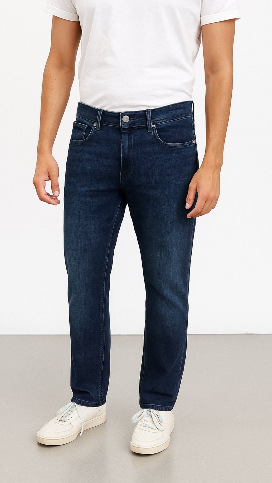 Person wearing dark blue jeans and a white shirt on a plain background