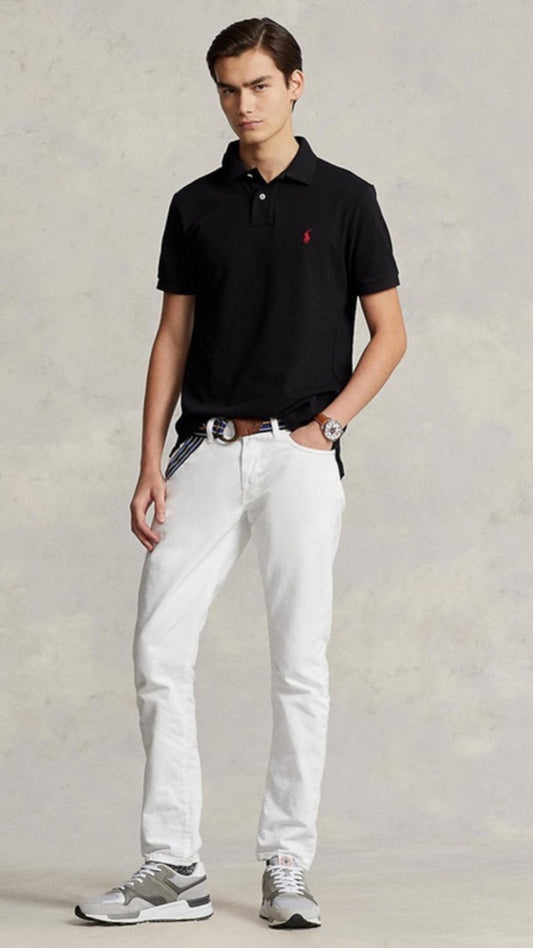 Man wearing a black polo shirt with a logo and white pants on a plain background