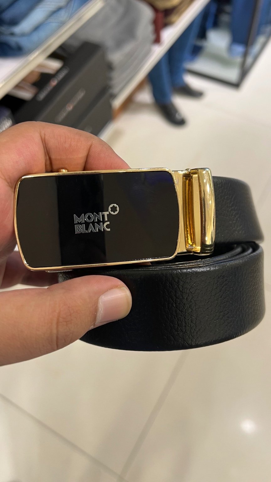 Black belt with gold buckle held by a hand, brand 'Montblanc' visible
