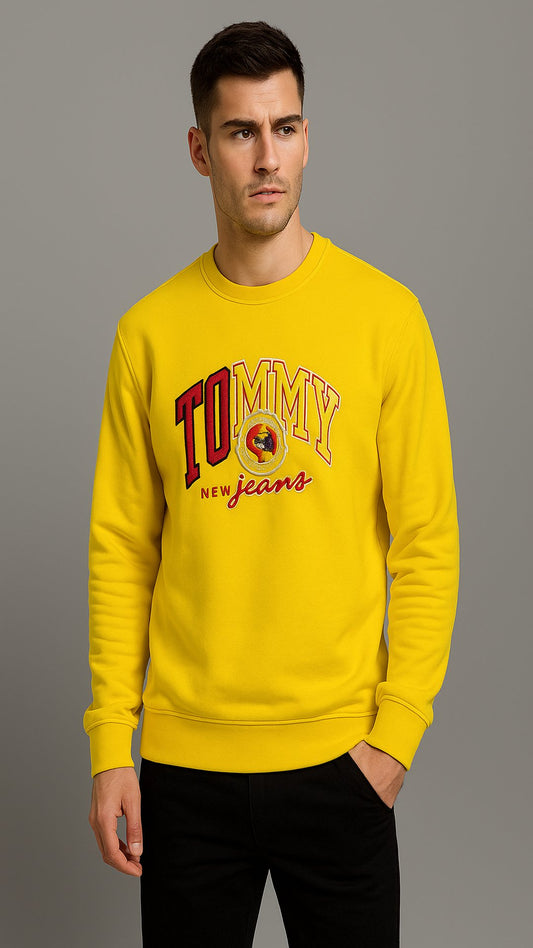 Man wearing a yellow Tommy Jeans sweatshirt against a gray background