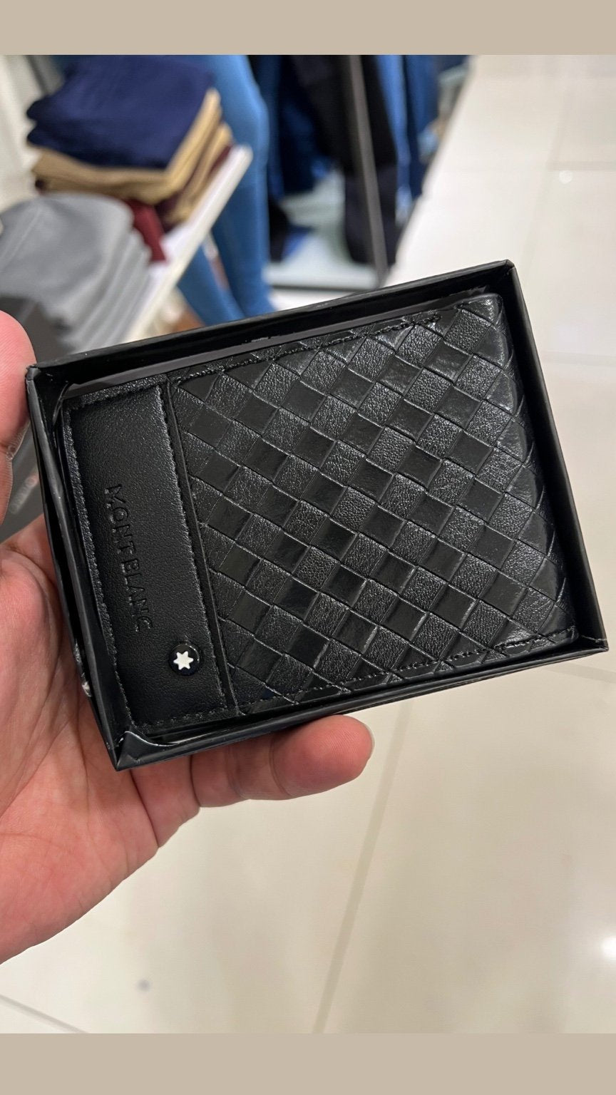 Black textured wallet held in a hand with a blurred background
