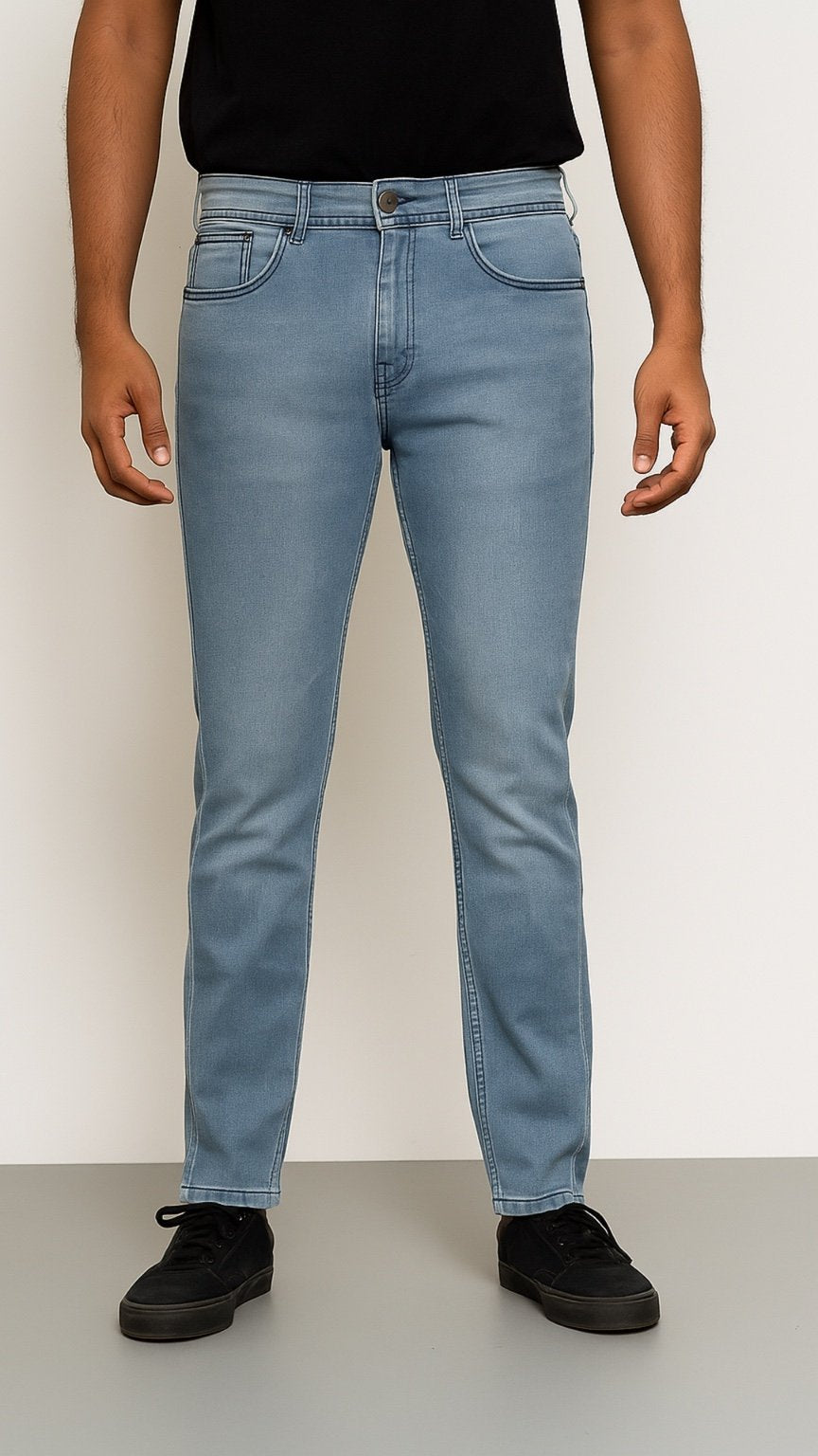 Person wearing light blue jeans and black shoes on a plain background