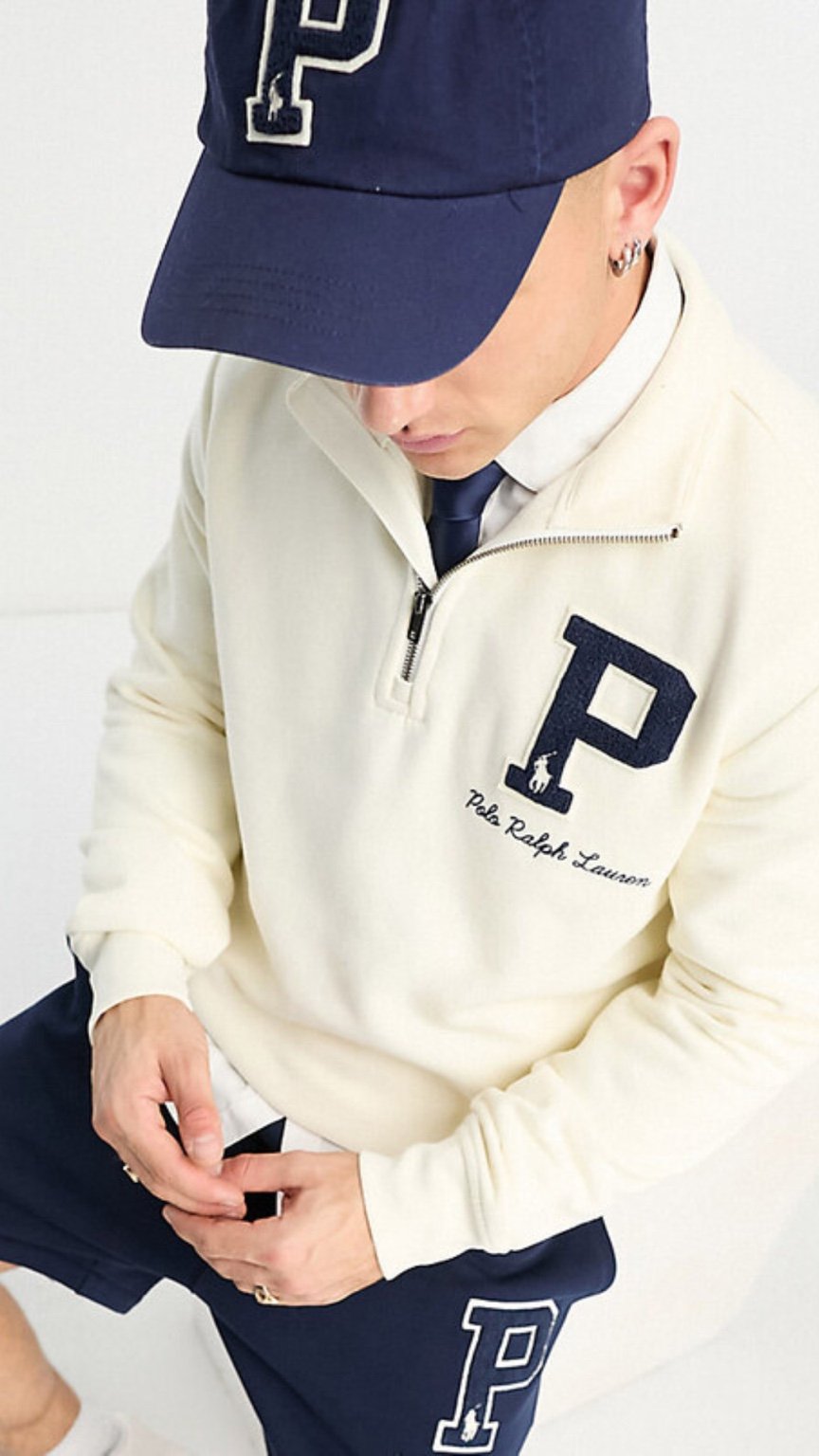 Person wearing a cream-colored half-zip sweatshirt with a large 'P' logo, paired with a navy cap and pants.