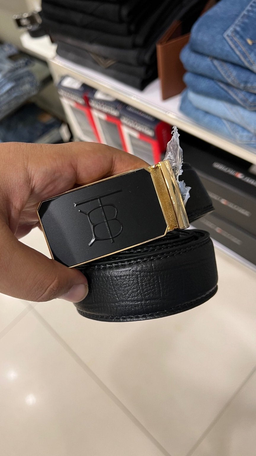 Black belt with gold buckle held by a hand in a store setting