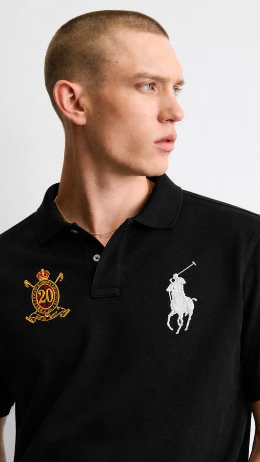 Man wearing a black polo shirt with logos on a plain background
