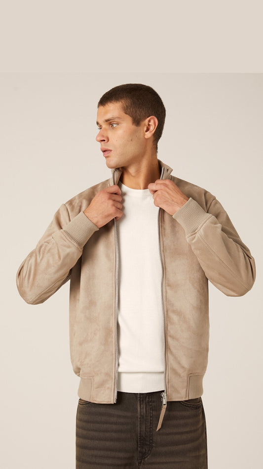Man wearing a beige bomber jacket over a white shirt on a plain background