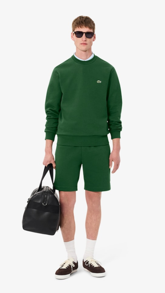 Man wearing a green outfit with sunglasses and a black bag on a white background