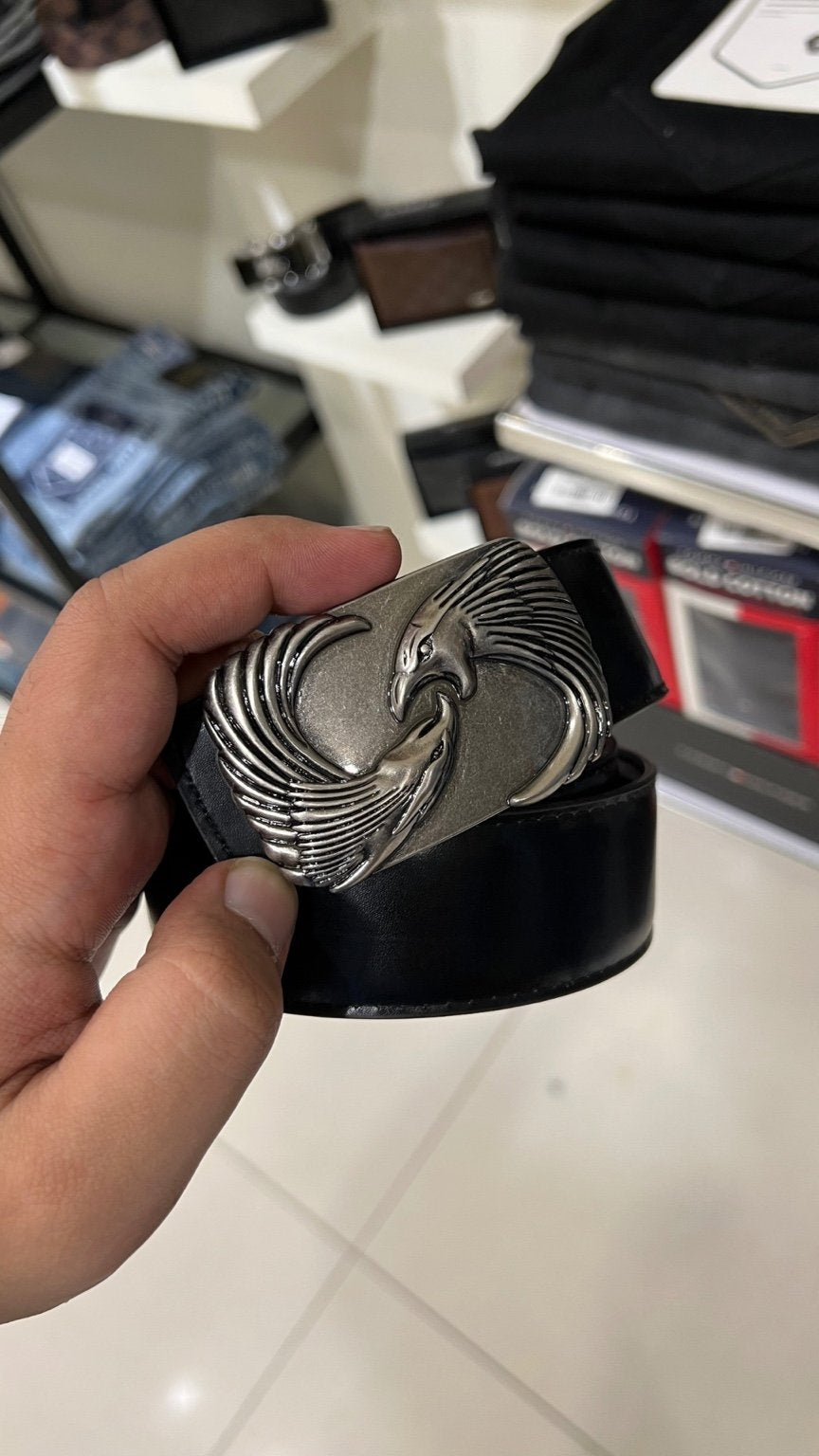 Hand holding a black belt with a silver buckle against a blurred indoor background