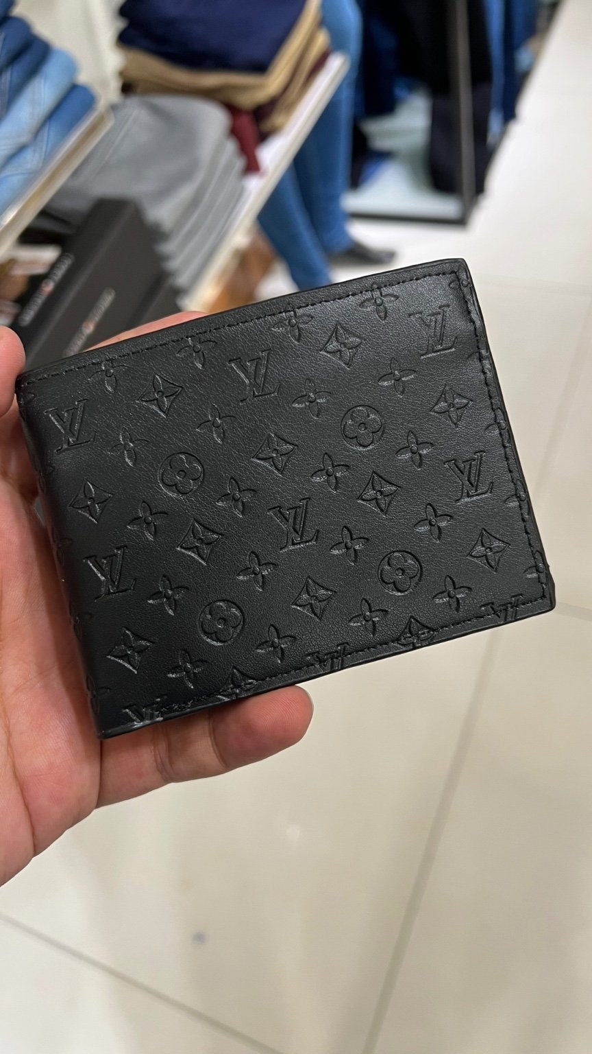 Black wallet with monogram pattern held by a hand on a blurred background