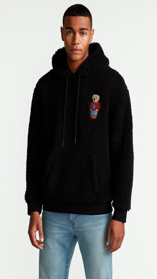 Person wearing a black hoodie with a teddy bear patch on a white background