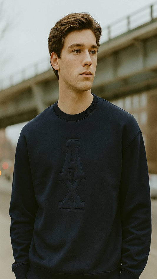 Man wearing a black sweatshirt with a logo, standing outdoors under a bridge.