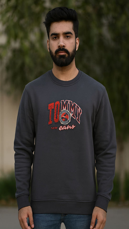 Man wearing a dark gray sweatshirt with a logo and text, standing outdoors.