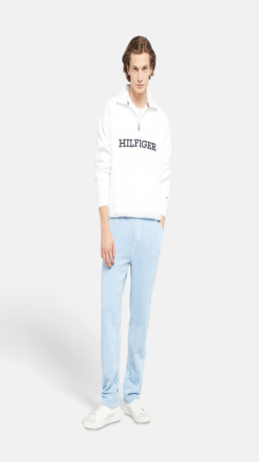 Person wearing a white Tommy Hilfiger hoodie and light blue pants on a white background