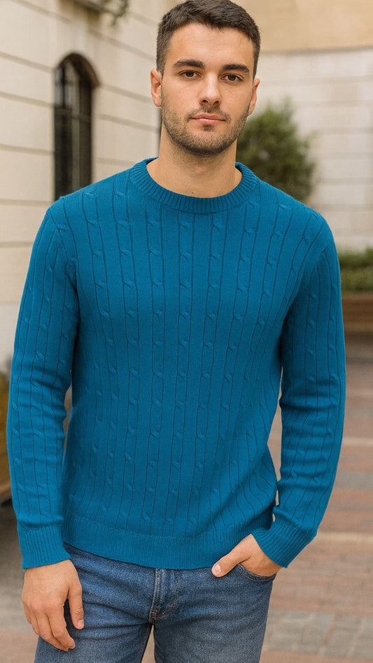 Man wearing a blue cable knit sweater and jeans standing outdoors.