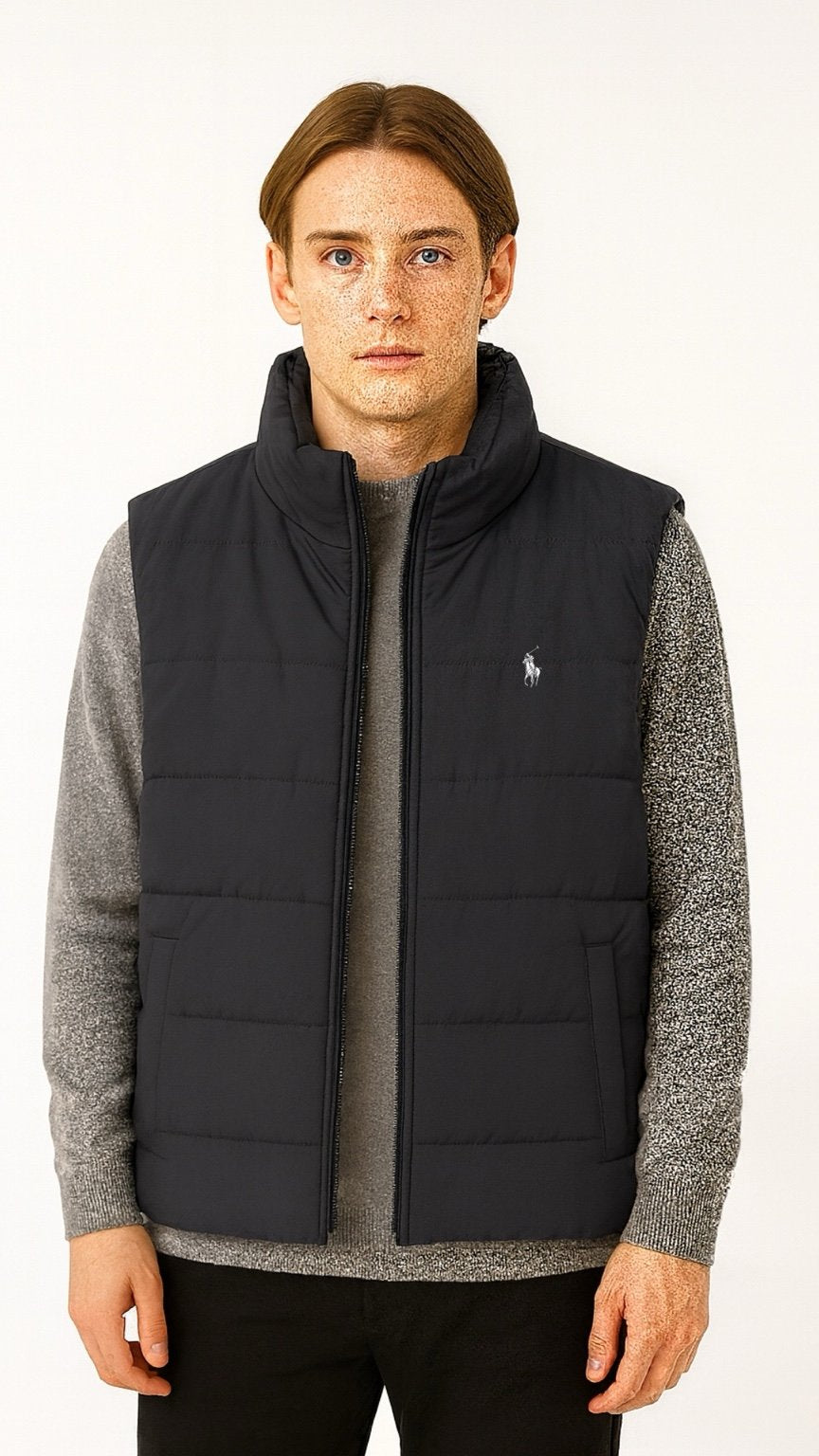 Man wearing a black quilted vest over a gray sweater on a white background