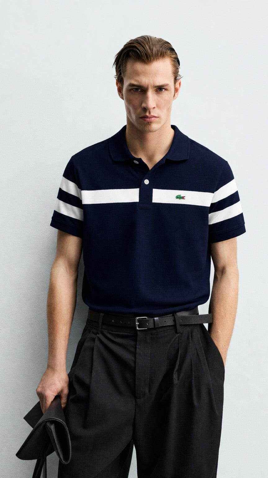 Man wearing a navy polo shirt with white stripes and a Lacoste logo, standing against a light gray background.
