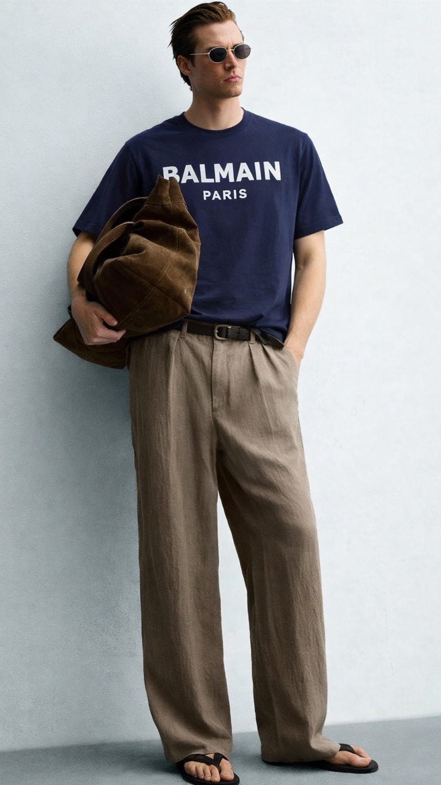Man wearing a navy Balmain t-shirt and brown pants against a gray background