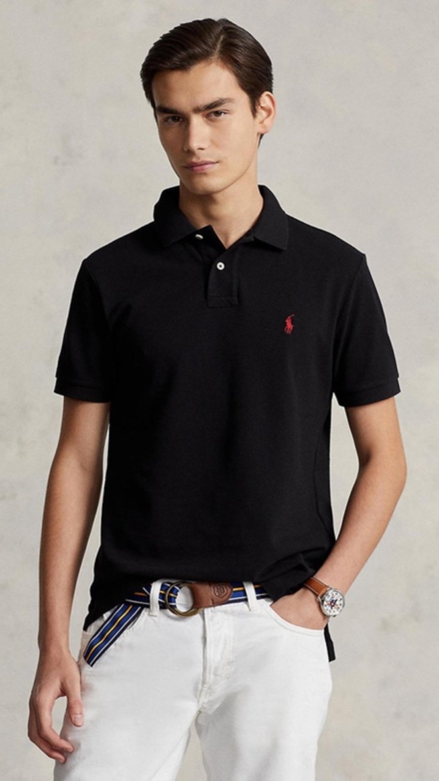 Man wearing a black polo shirt with a red logo, white pants, and a belt on a plain background
