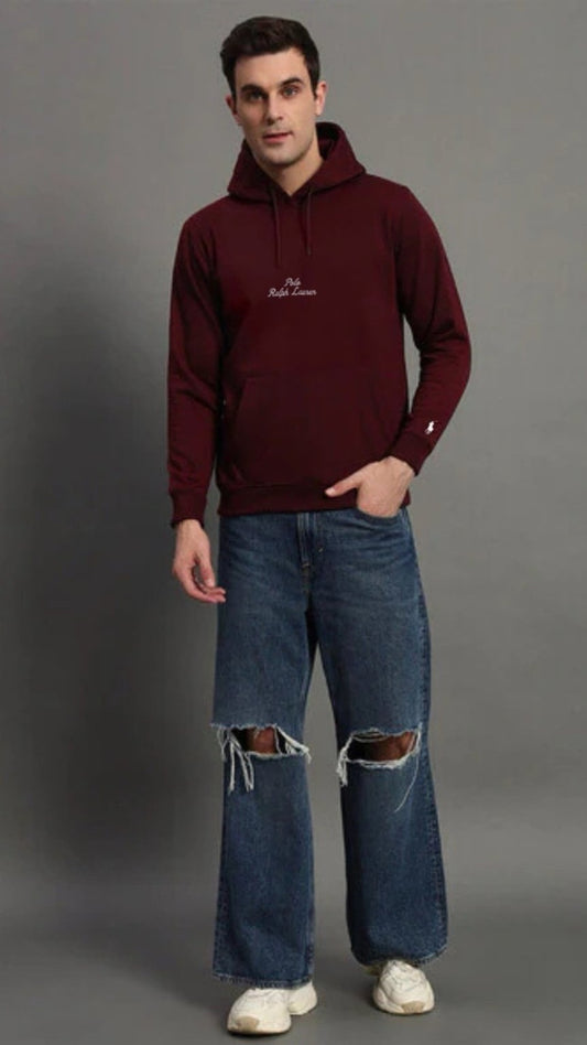 Man wearing a burgundy hoodie and ripped jeans on a gray background