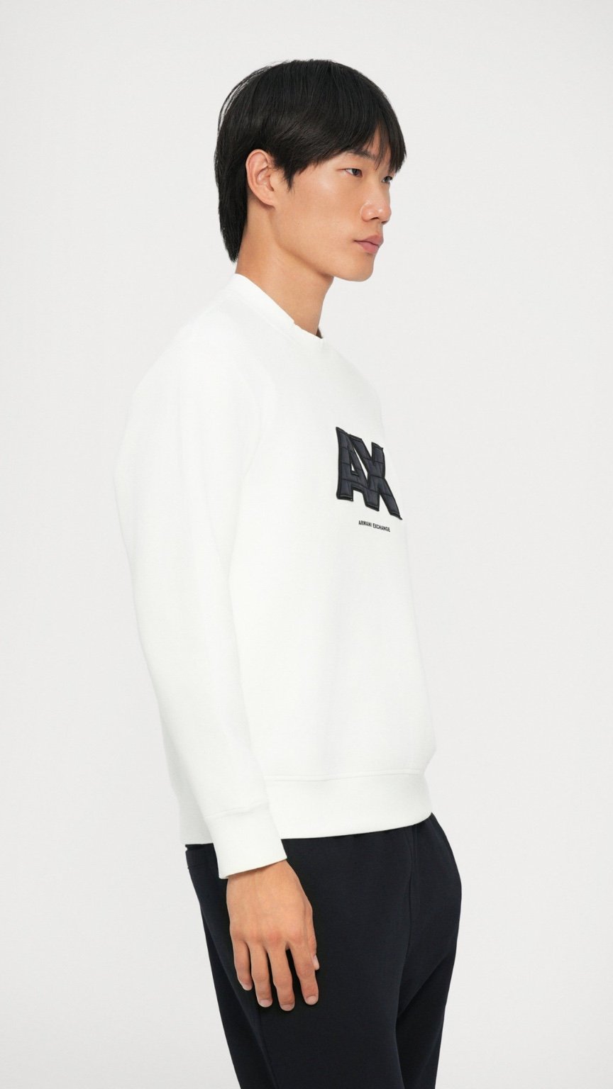 Person wearing a white sweater with a logo on a plain background
