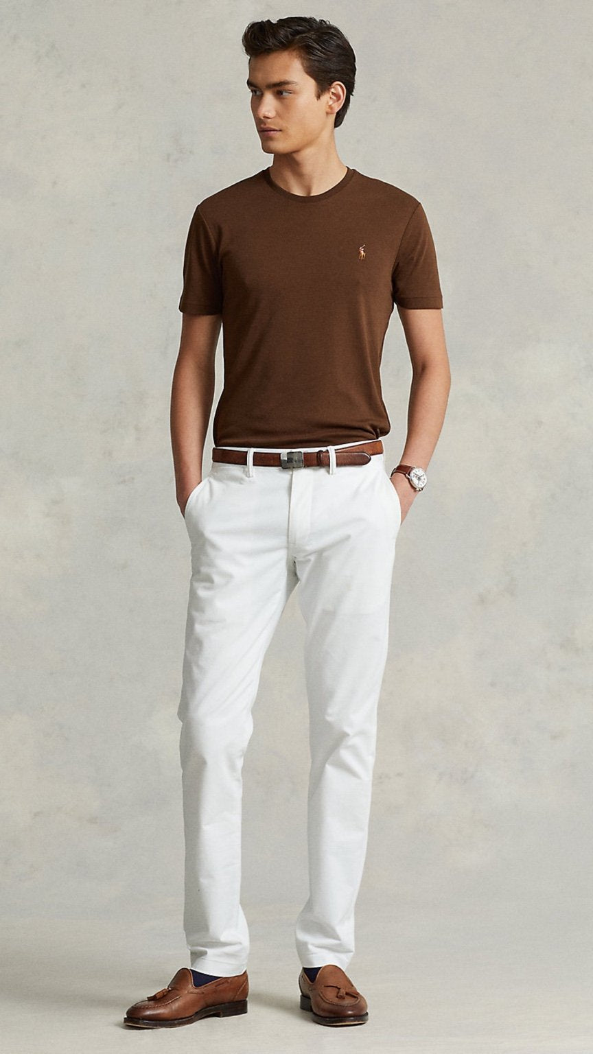 Man wearing a brown t-shirt, white pants, and brown shoes against a neutral background