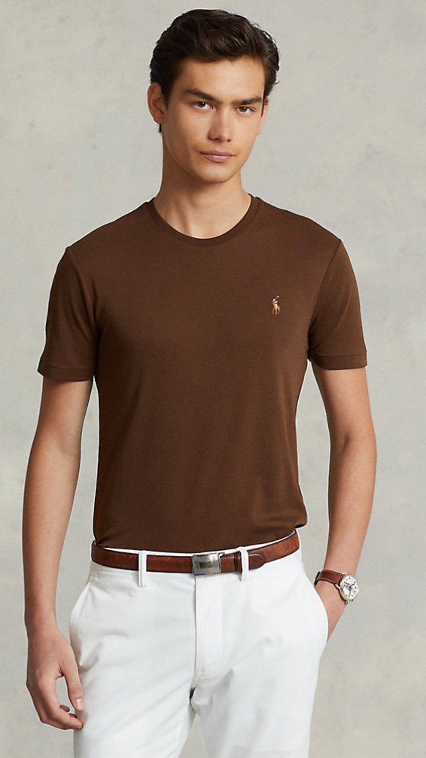 Man wearing a brown t-shirt with a logo, white pants, and a watch on a plain background