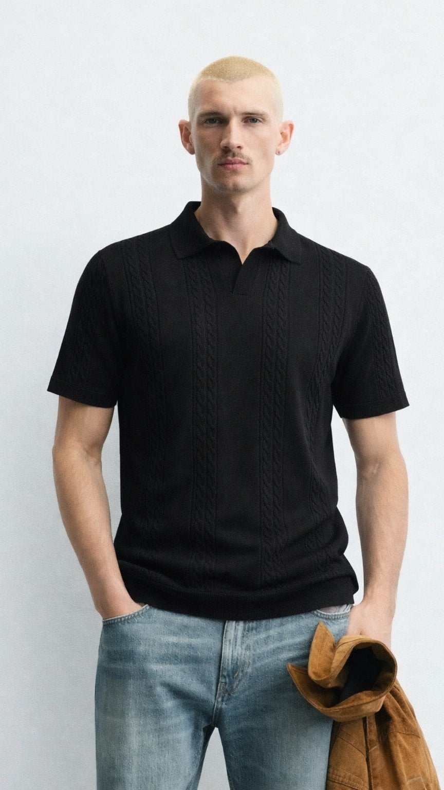 Man wearing a black polo shirt and blue jeans against a white background