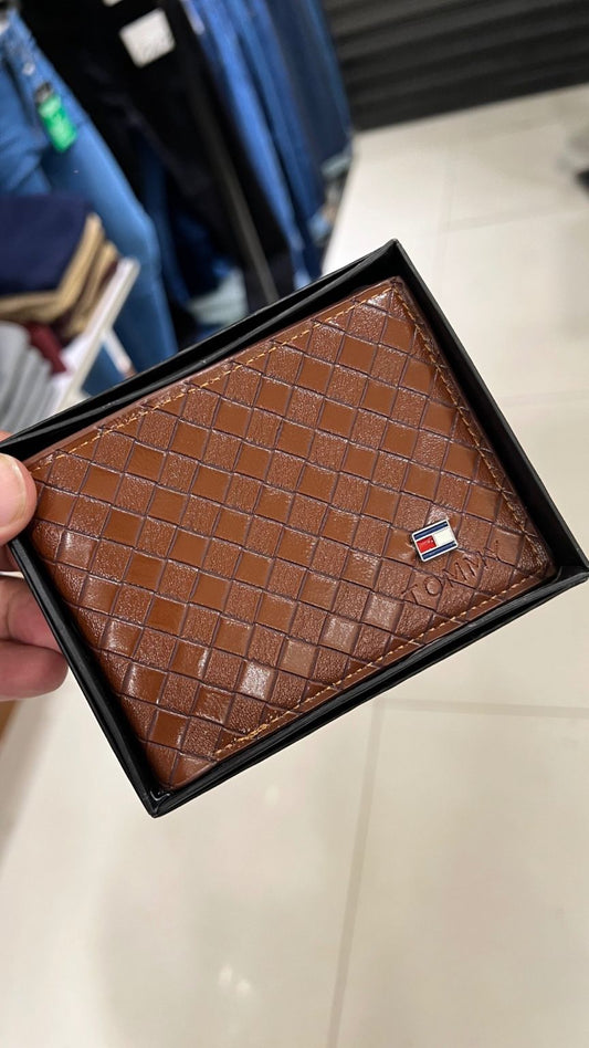 Brown textured wallet with a brand logo held in front of a blurred background