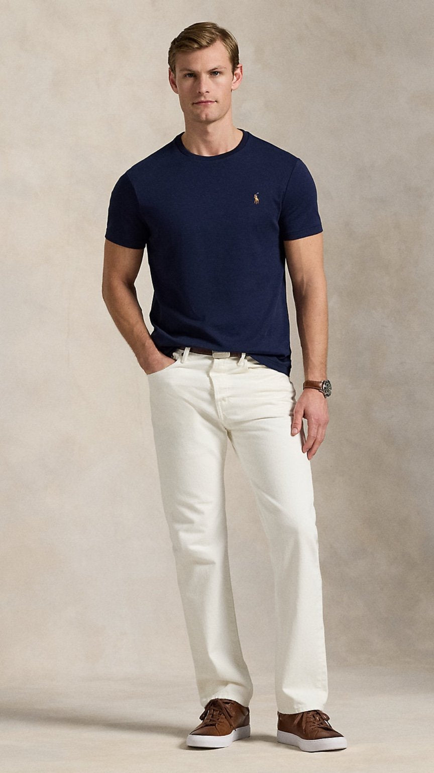 Man wearing a navy blue t-shirt, white pants, and brown shoes against a beige background