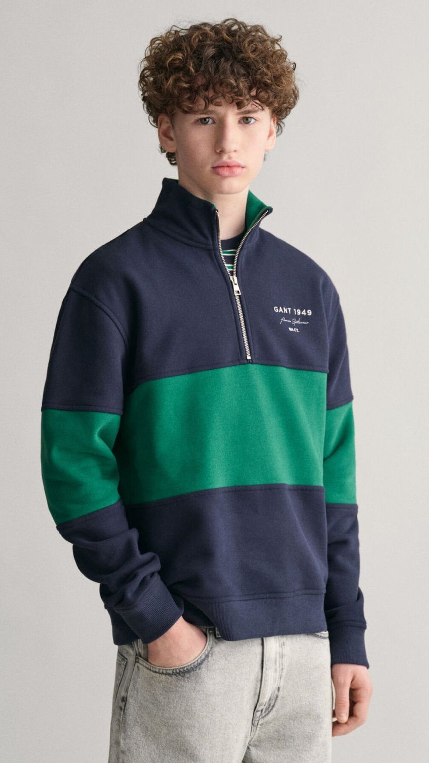 Person wearing a navy and green color-blocked pullover with a visible brand logo on a plain background