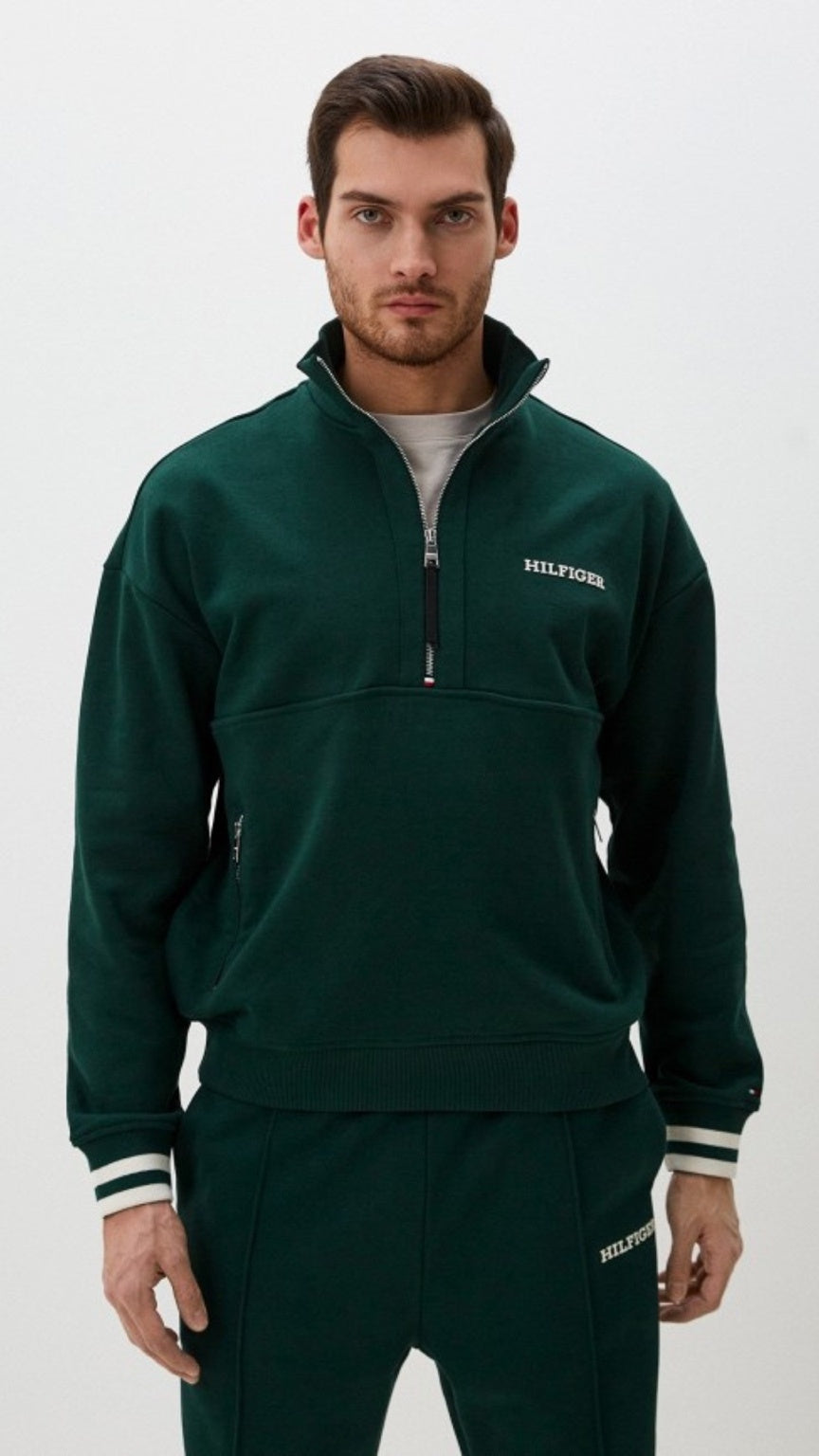 Man wearing a green pullover with a visible brand logo on a white background