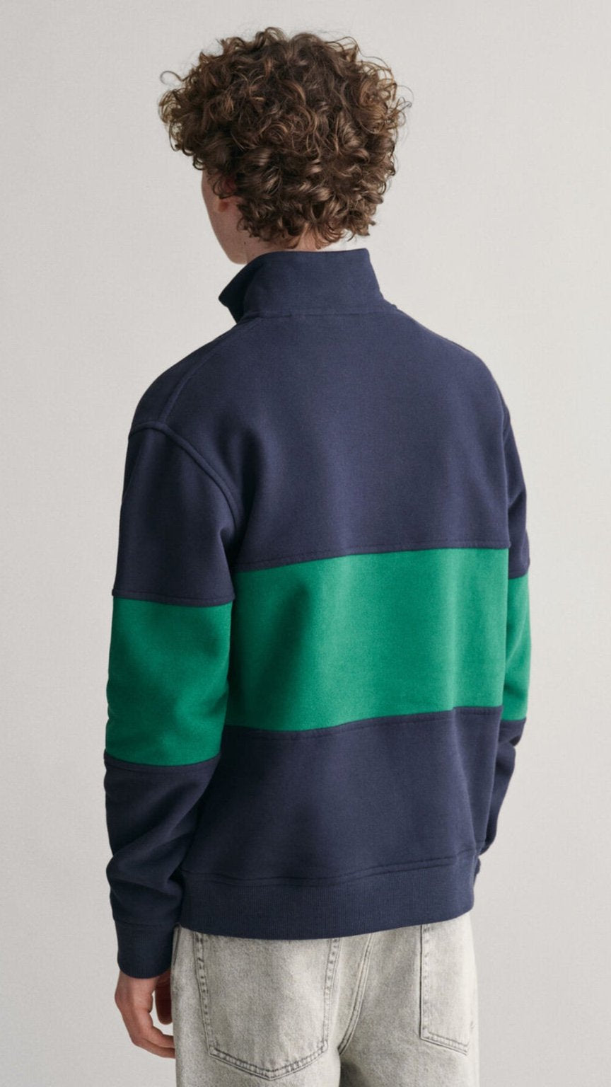 Person wearing a navy and green color-blocked sweater on a plain background
