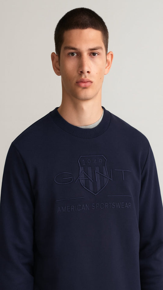 Man wearing a navy blue sweatshirt with a brand logo on a plain background