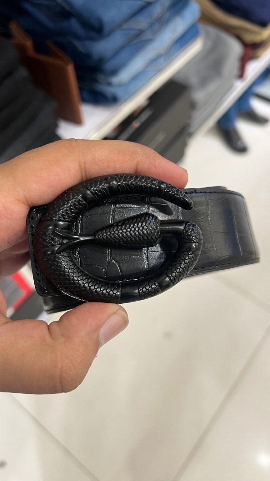 Black leather belt with a complex buckle held by a hand on a blurred background