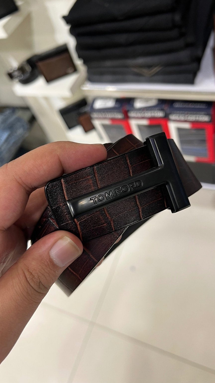 Hand holding a brown leather belt with a visible brand logo.