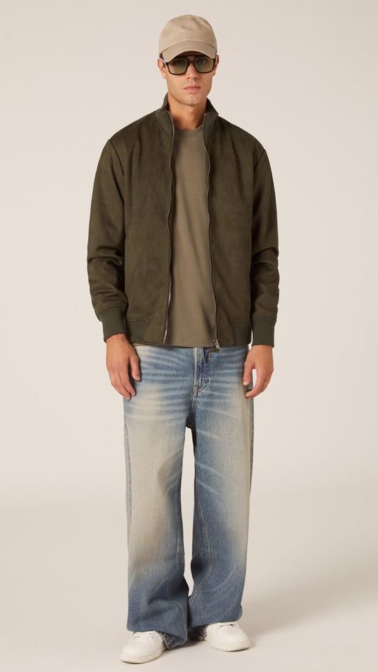 Man wearing a green jacket, brown shirt, blue jeans, and white sneakers on a plain background