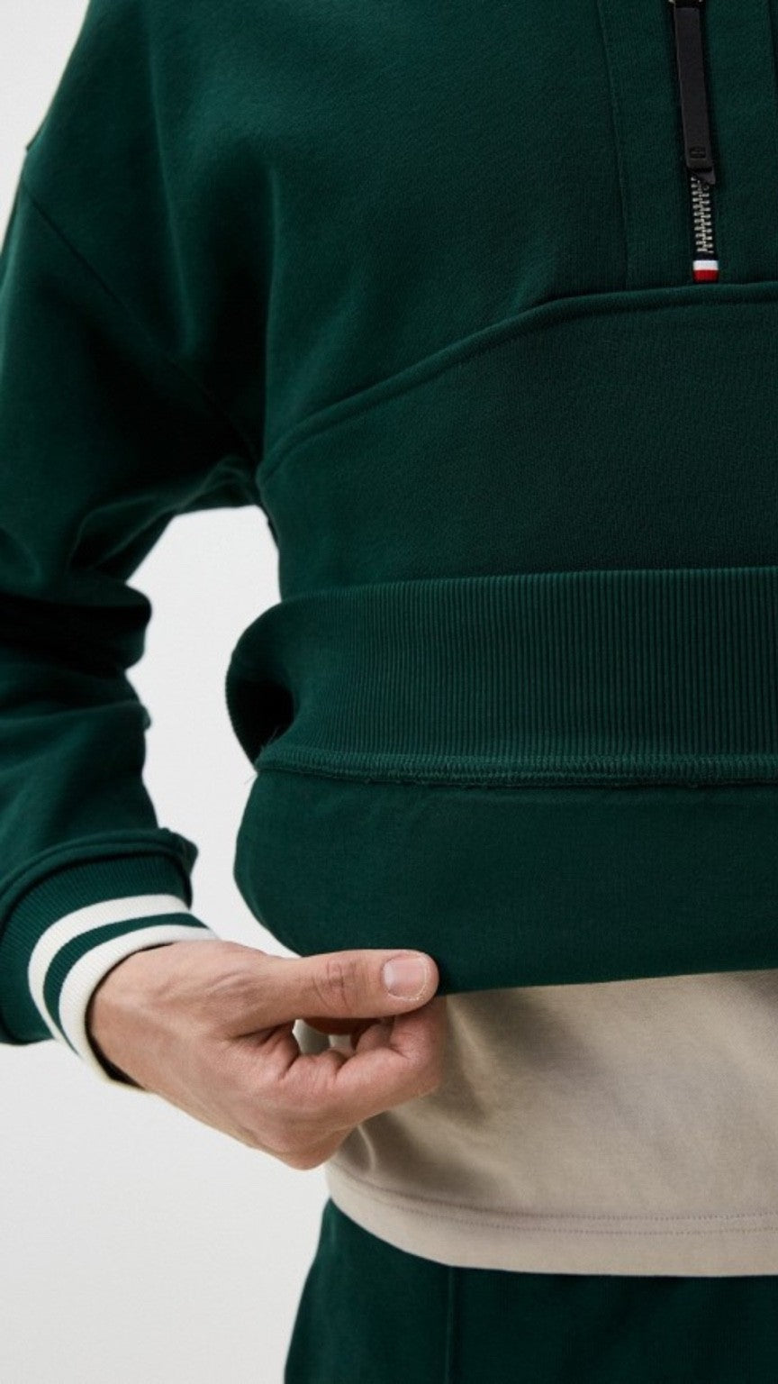 Close-up of a person wearing a green jacket with a zipper, on a light gray background.