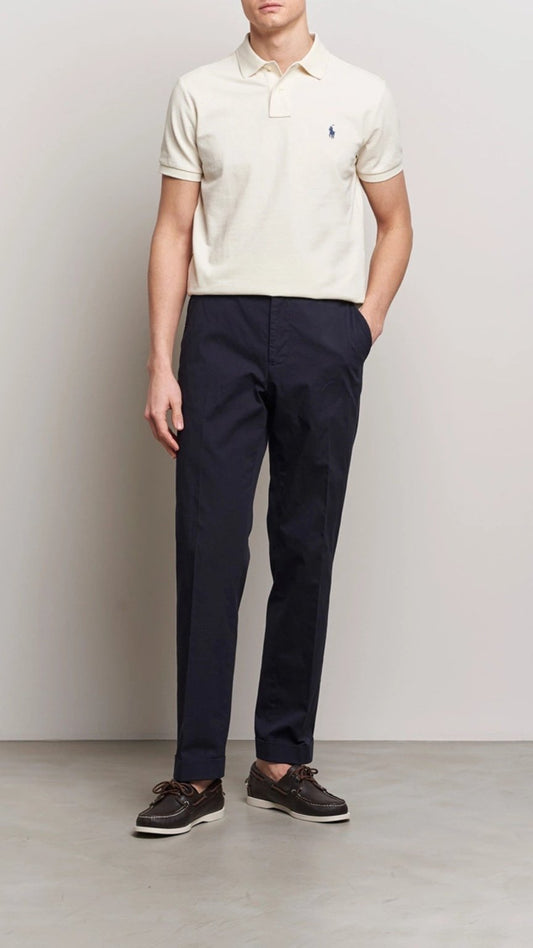 Person wearing a white polo shirt and navy pants against a plain background