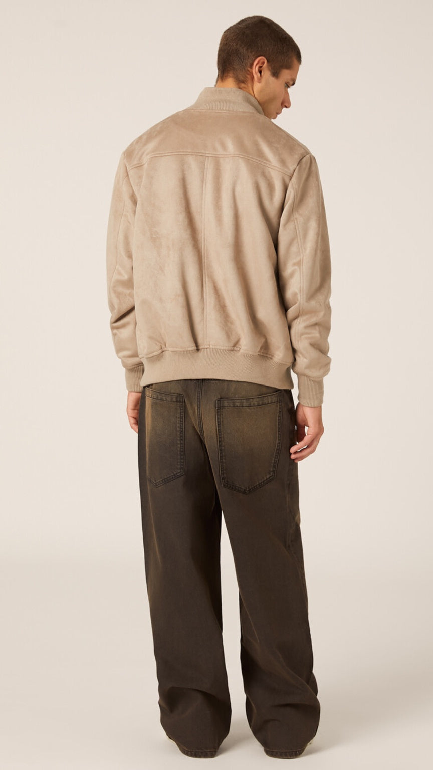 Man wearing a beige jacket and dark pants on a plain background