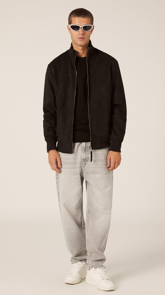 Man wearing a black jacket, gray pants, and white sneakers on a plain background