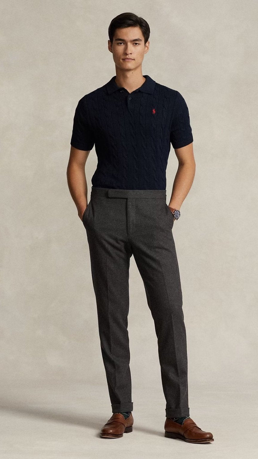 Man wearing a navy polo shirt and gray pants against a beige background