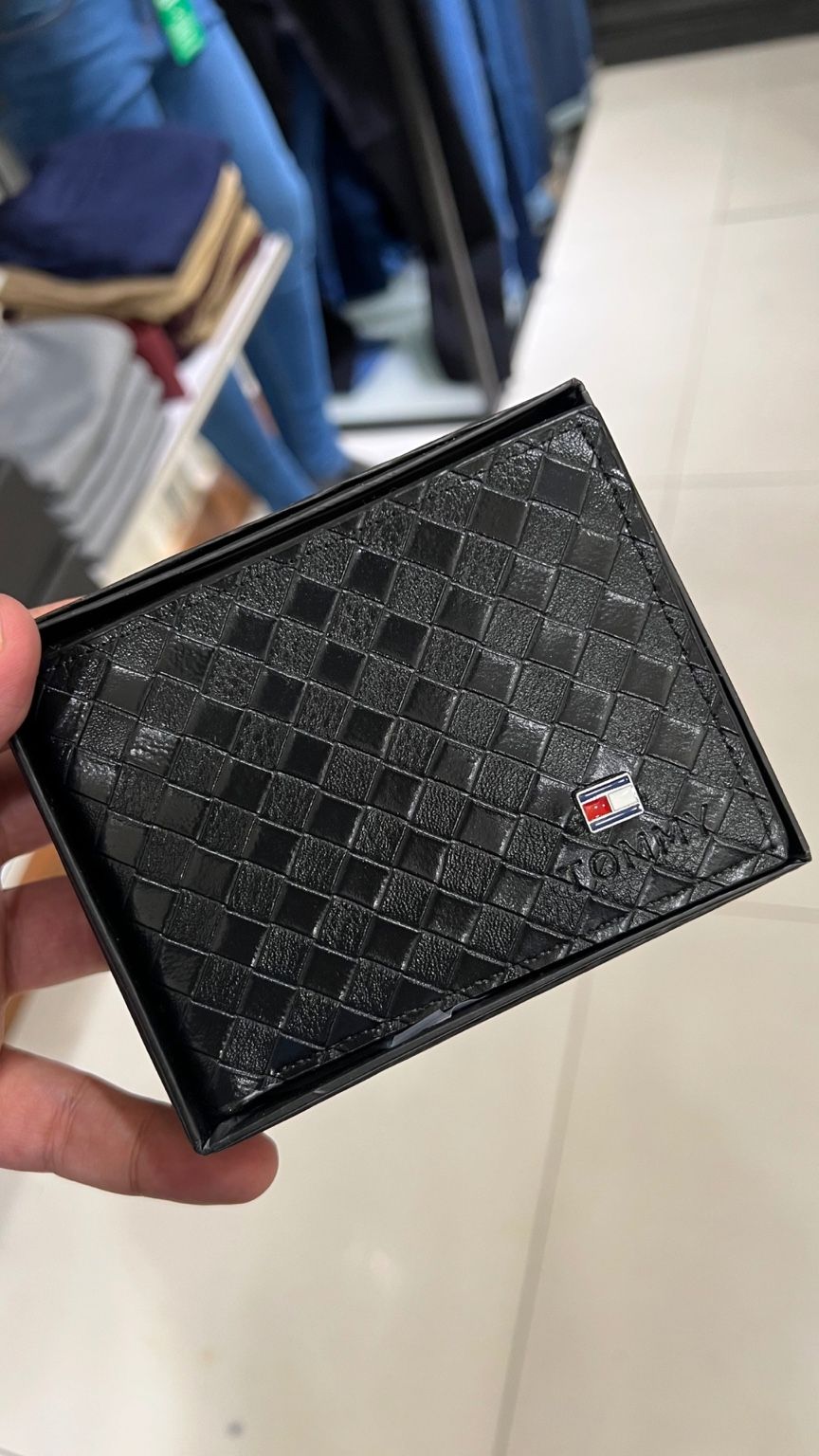 Black checkered wallet held by a hand with a blurred background