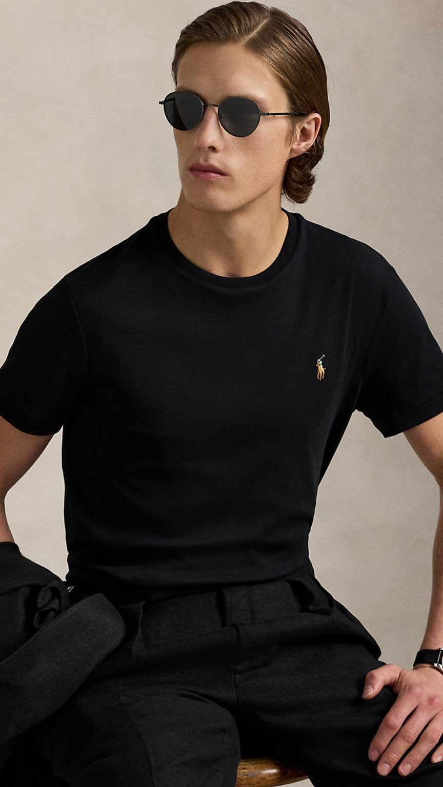 Man wearing a black t-shirt with a logo and sunglasses, sitting against a neutral background