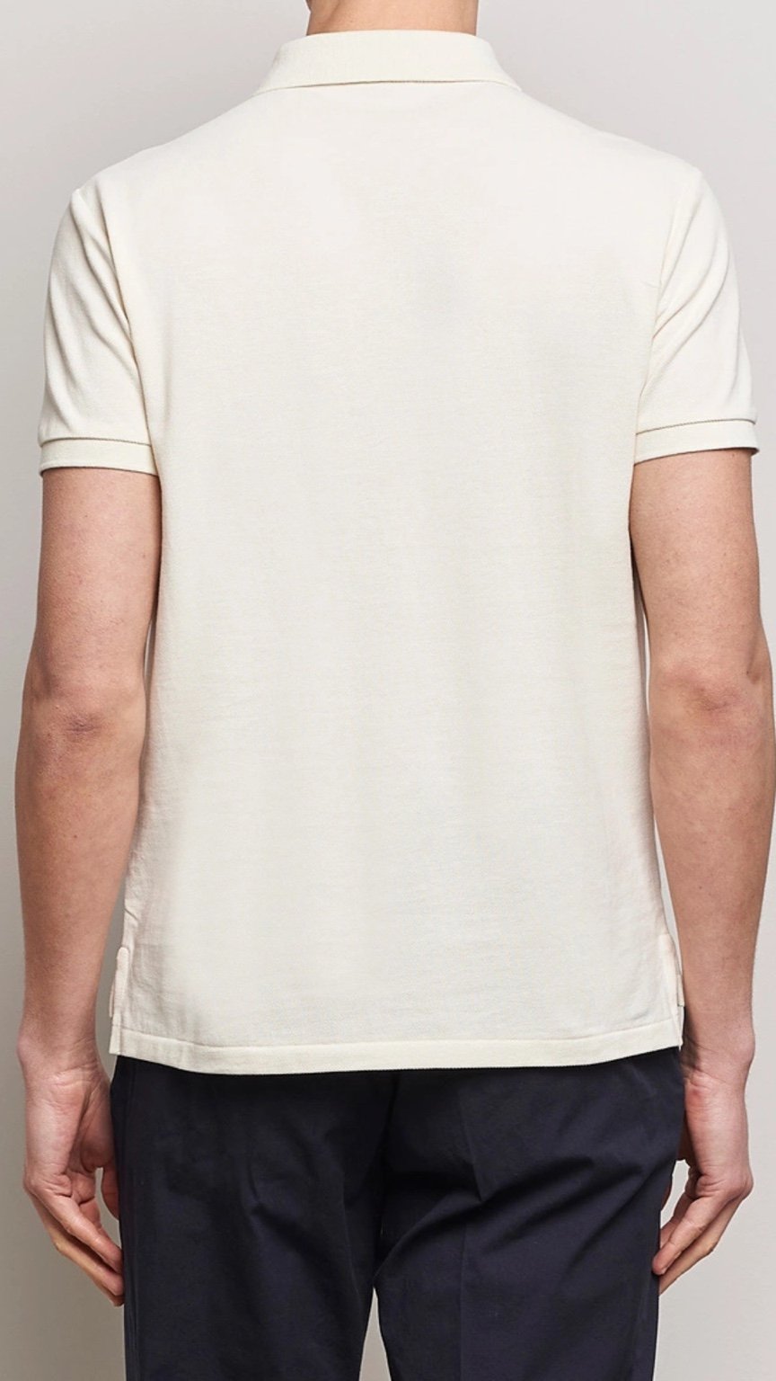 Person wearing a light-colored polo shirt and dark pants on a plain background