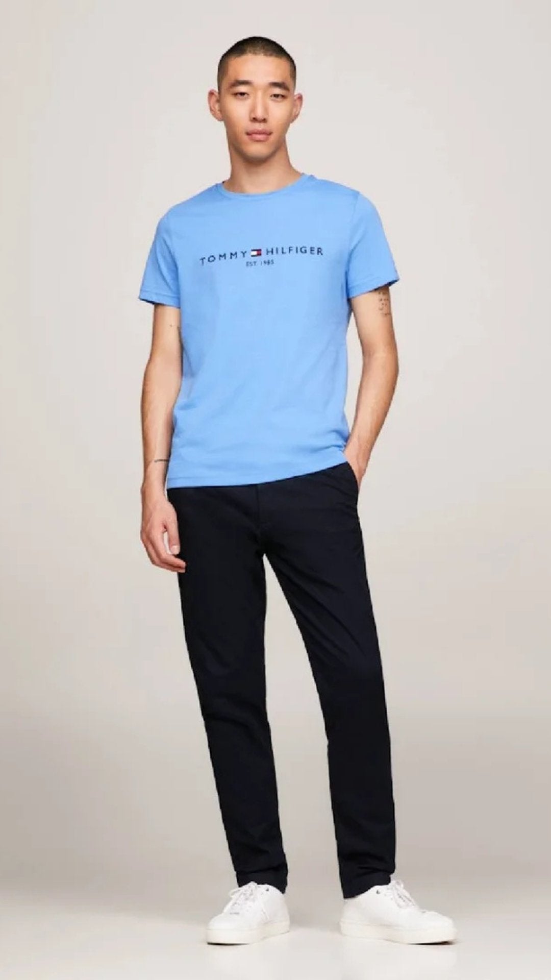 Person wearing a blue Tommy Hilfiger t-shirt and black pants on a white background