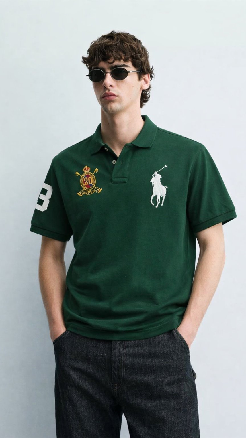 Man wearing a green polo shirt with logos on a light gray background