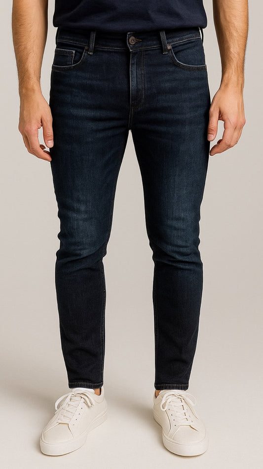 Person wearing dark blue jeans and white sneakers on a plain background