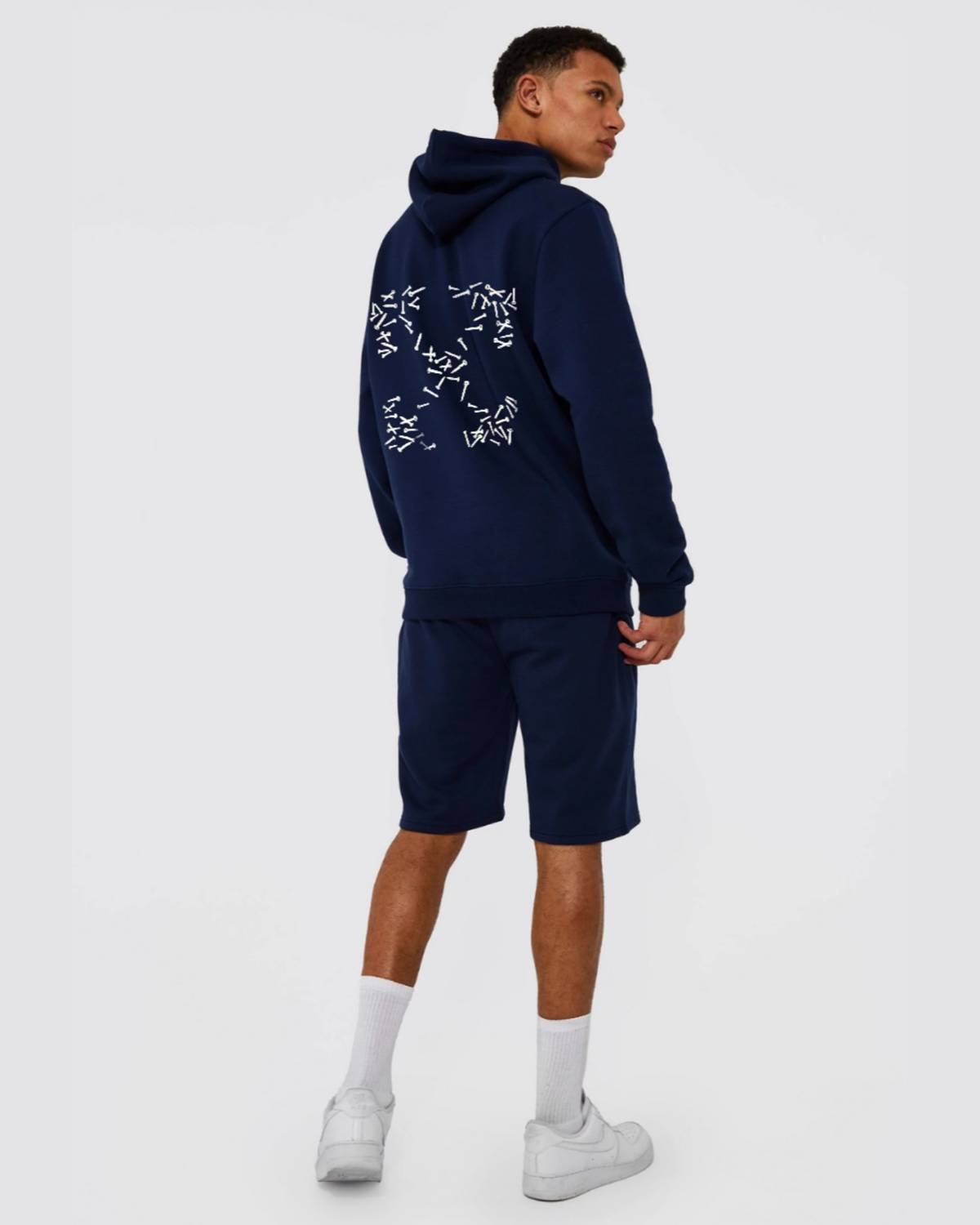 Person wearing a navy hoodie and shorts set with white designs on a white background