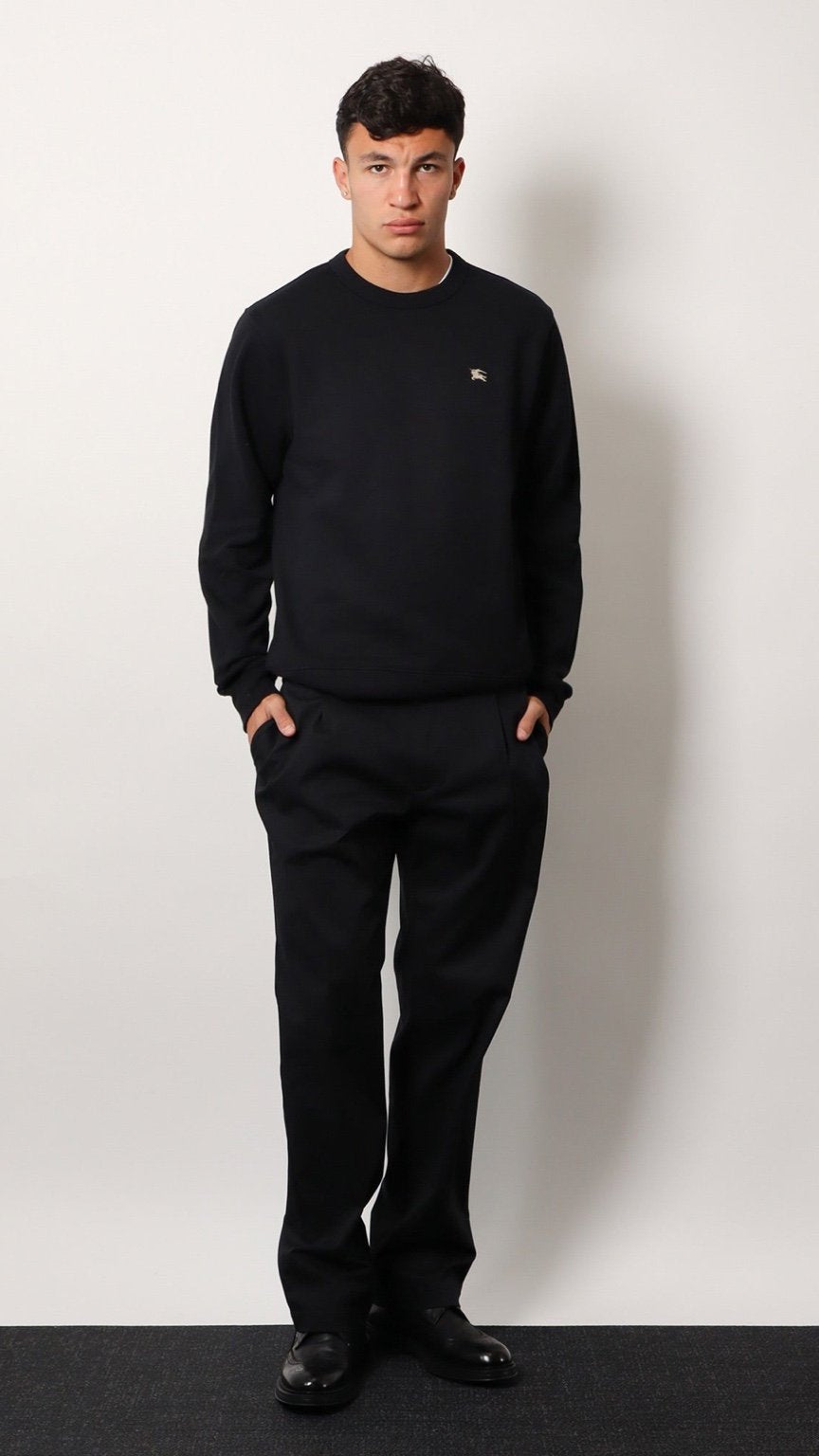 Man wearing a black outfit with a small logo on a white background